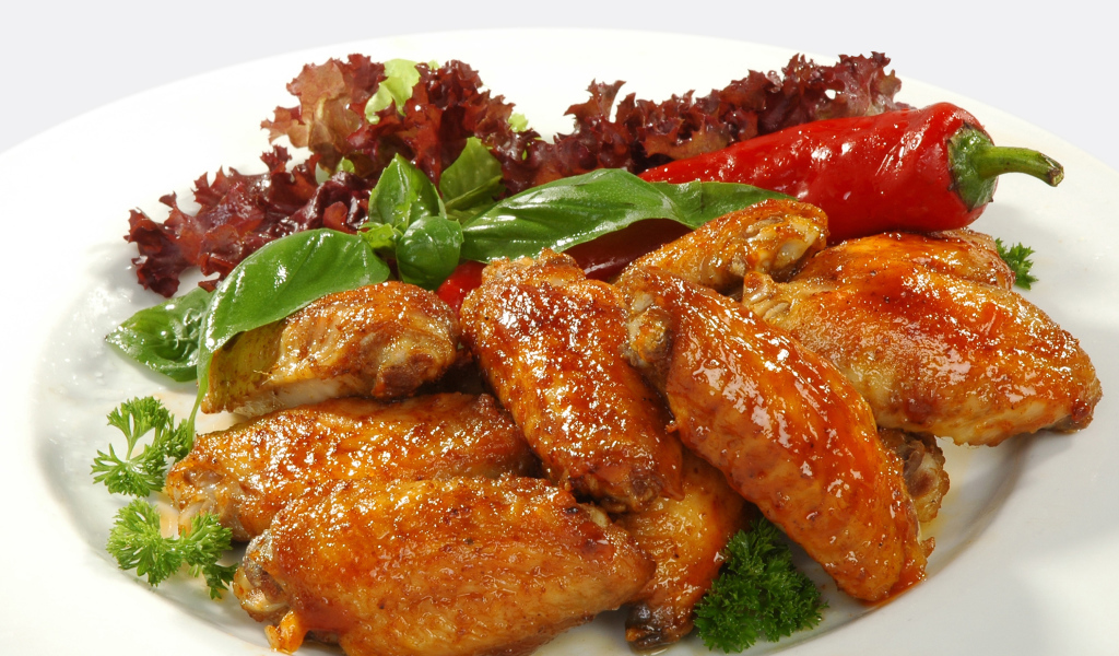Жареные куриные крылышки на тарелке с острым перцем и зеленью 