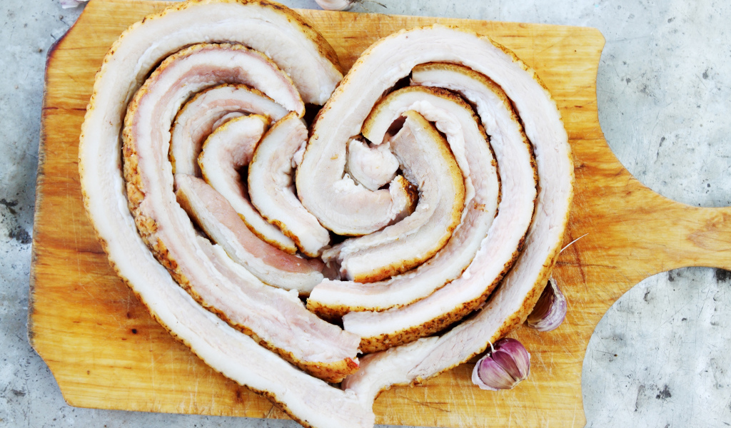 Сердце из свежего сала на доске с чесноком