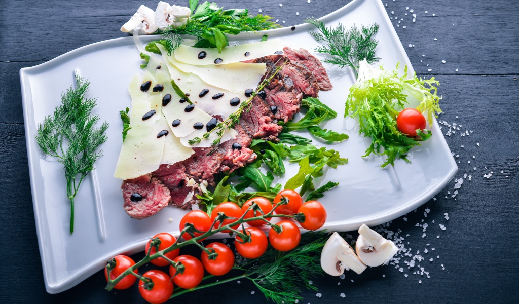 Мясо с сыром, овощами и зеленью на тарелке
