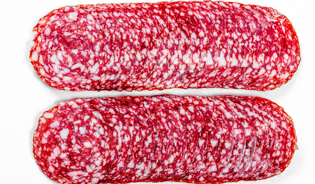 Колбаса салями нарезанная тонкими кусочками на белом фоне