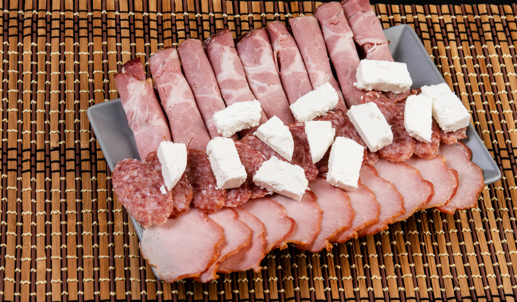 Колбаса и ветчина на тарелке с кусочками сыра фета