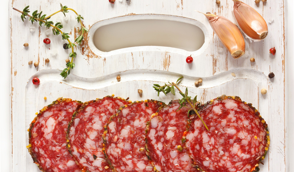 Нарезанная колбаса на разделочной доске со специями и чесноком