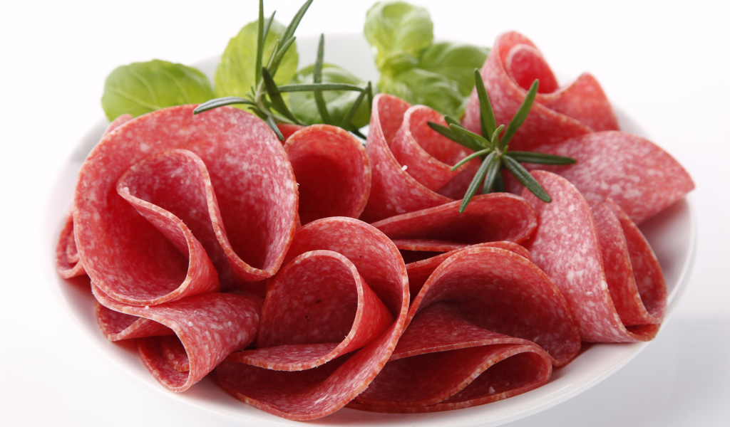 Тонкие кусочки колбасы на тарелке с зеленью 