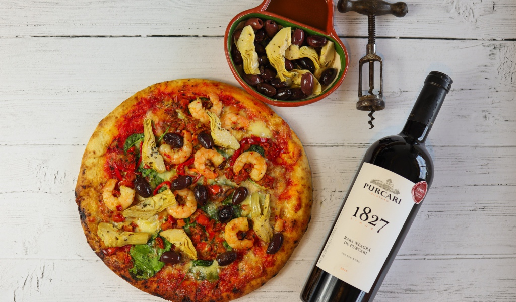 Пицца на столе с оливками и бутылкой вина