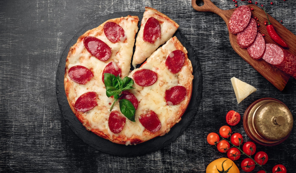 Пицца с сыром и салями на столе с помидорами и колбасой
