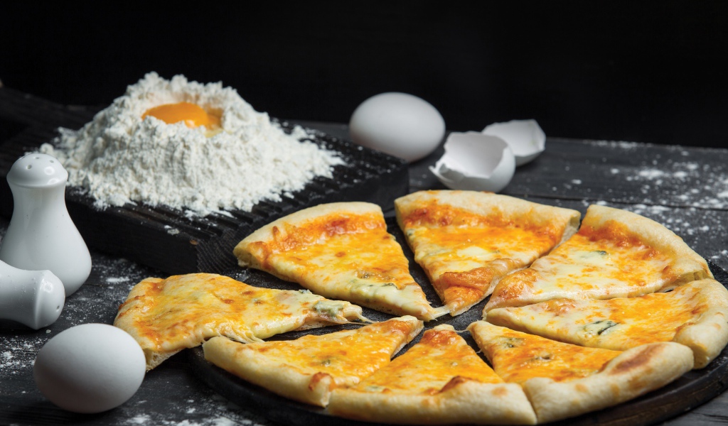 Пицца с сыром нарезана кусочками на столе с мукой и яйцами