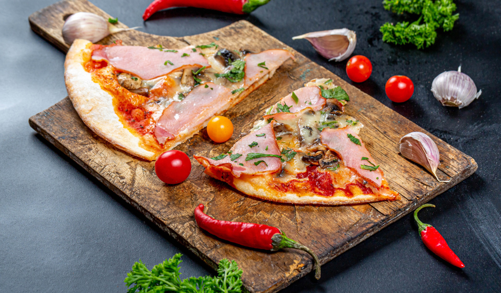 Два куска пиццы на разделочной доске с красным перцем и чесноком