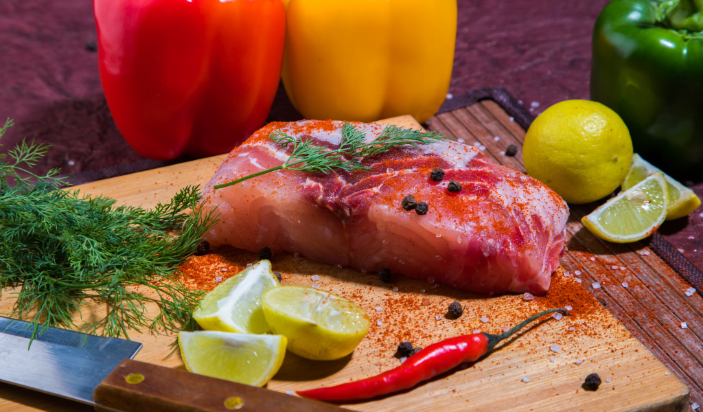Кусок сырой рыбы на разделочной доске со специями, лимоном и болгарским перцем