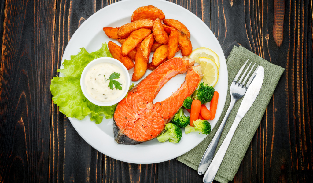 Кусок красной рыбы на тарелке с картофелем и соусом