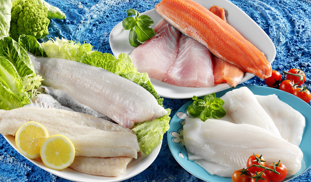 Филе рыбы на тарелках с помидорами и листьями салата