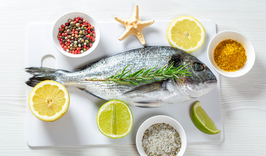 Свежая рыба на доске с солью, перцем, куркумой и лимоном