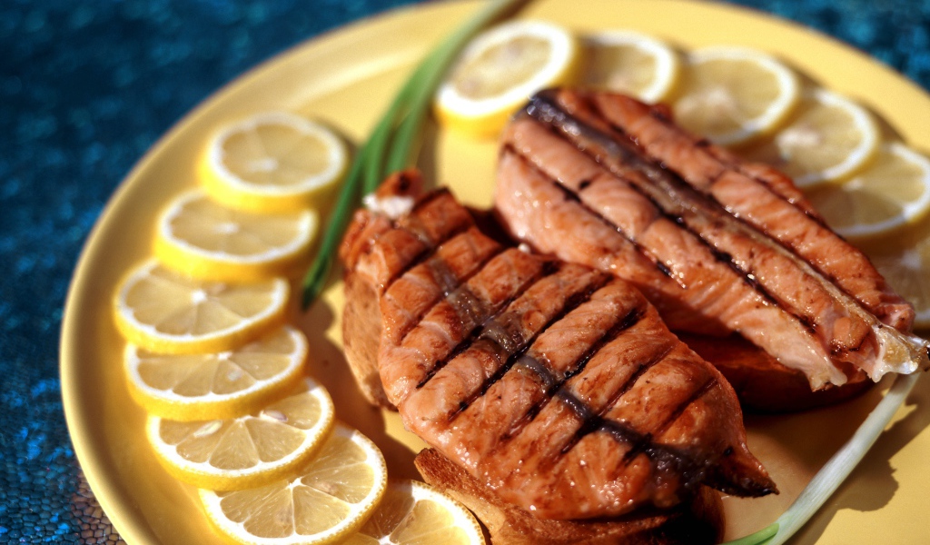 Зажаренная красная рыба с кусочками лимона и зеленым луком