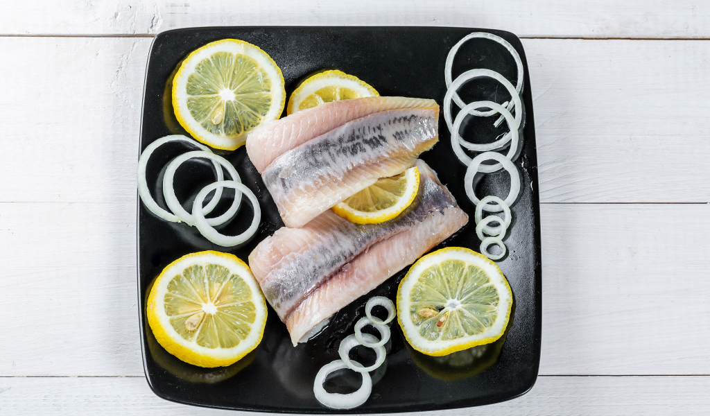 Филе сельди на черной тарелке с луком и лимоном
