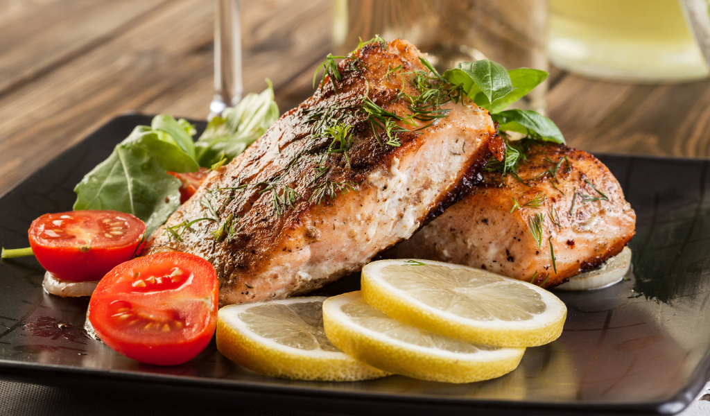 Куски запеченной рыбы на тарелке с помидорами и лимоном