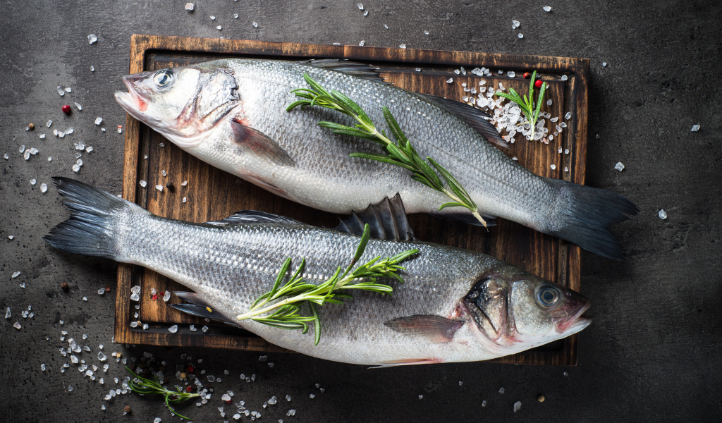 Две свежие рыбины на разделочной доске с солью и веточками розмарина