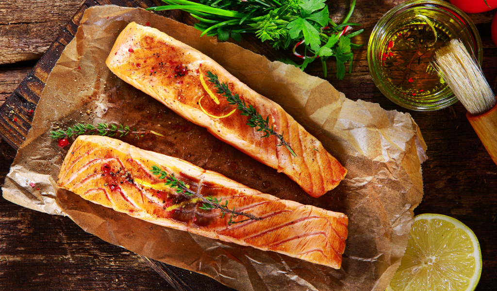 Два куска запеченной рыбы на столе с оливковым маслом и зеленью