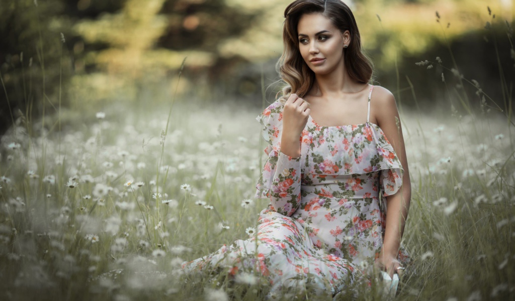 Красивая девушка в сарафане сидит на поляне с ромашками 