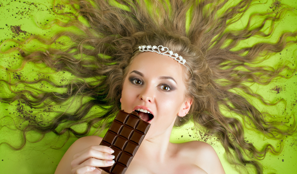 Красивая девушка с украшением в волосах лежит с шоколадкой 