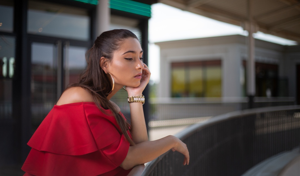 Задуманная девушка в красном платье стоит у перил 