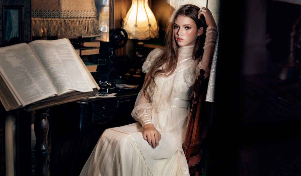 Девушка в красивом белом платье сидит на стуле у стола