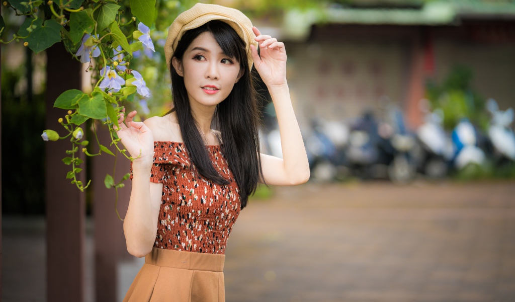 Молодая девушка азиатка в кепке стоит у голубых цветов