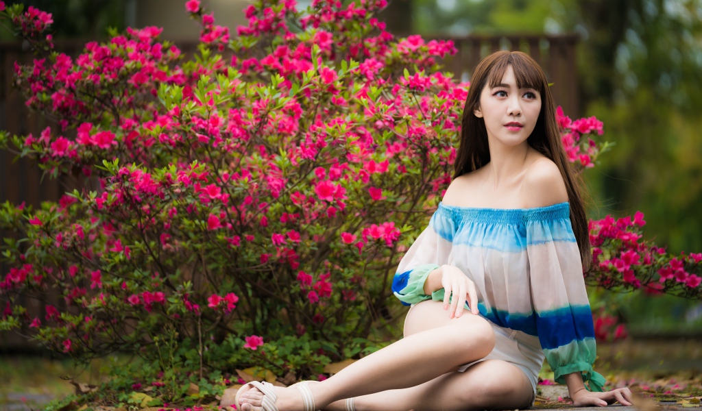 Молодая девушка азиатка сидит у куста с розовыми цветами