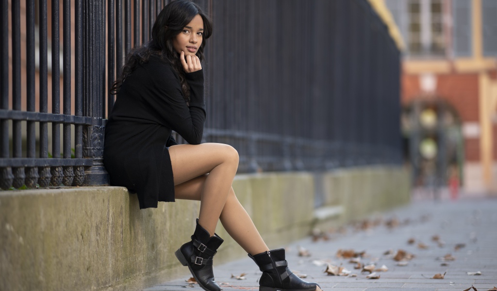 Молодая девушка в черном сидит у железного забора