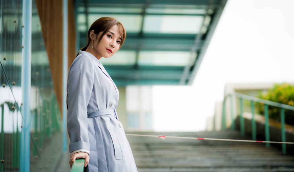 Девушка азиатка в пальто стоит у перил 