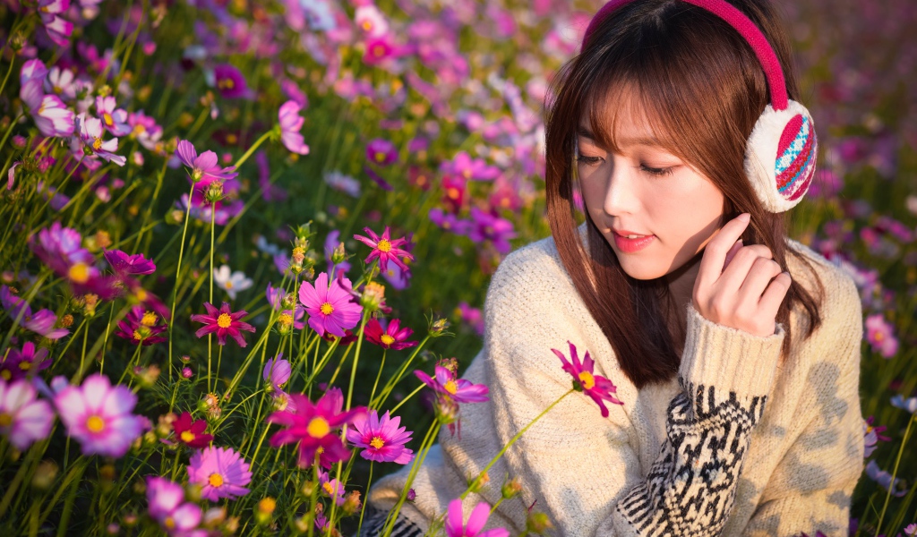 Девушка азиатка в наушниках сидит в цветах космеи