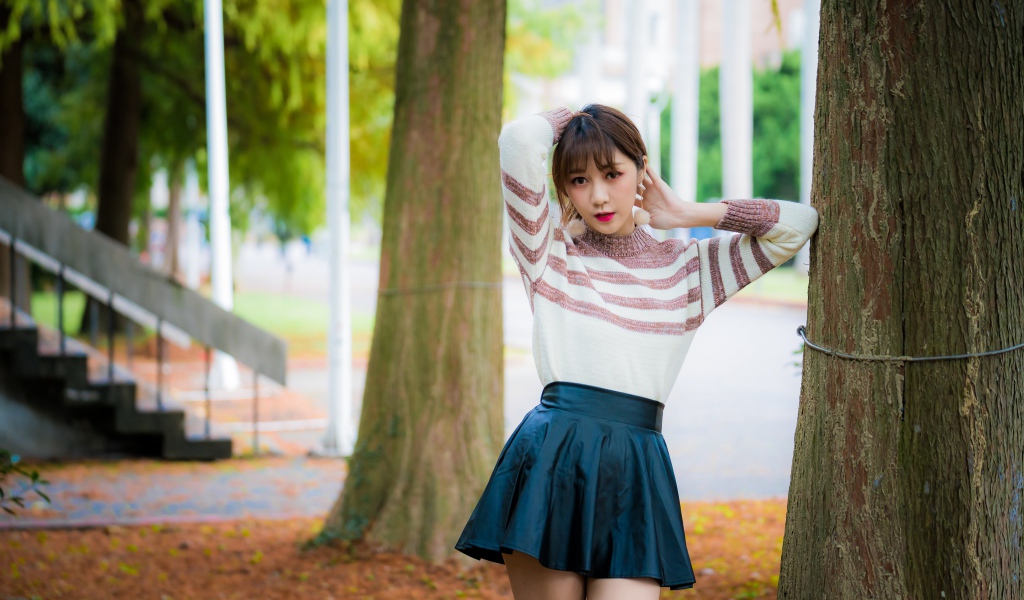 Девушка азиатка стоит в короткой юбке у дерева