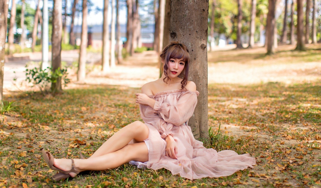 Красивая девушка азиатка в платье сидит под деревом