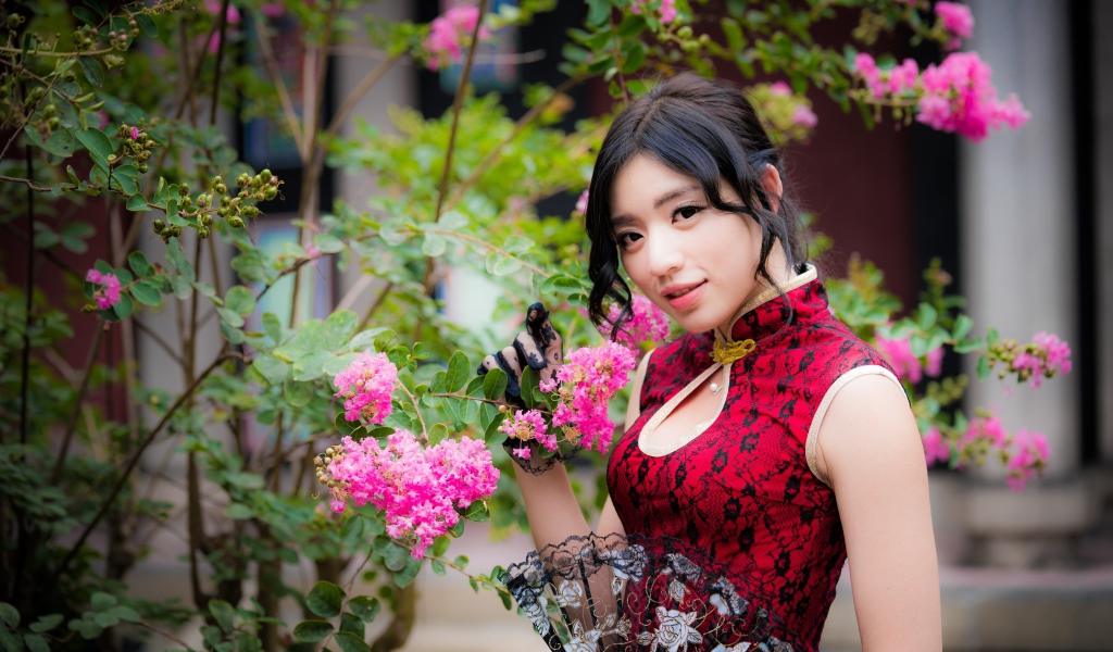 Красивая азиатка с веером в руках стоит у куста с розовыми цветами