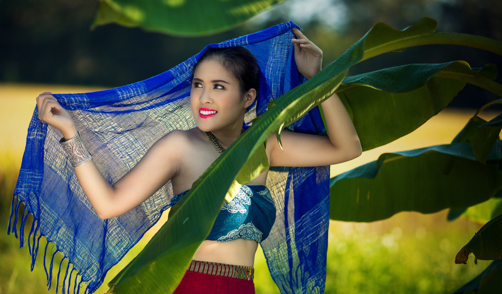 Красивая девушка азиатка с синим палантином у зеленых листьев