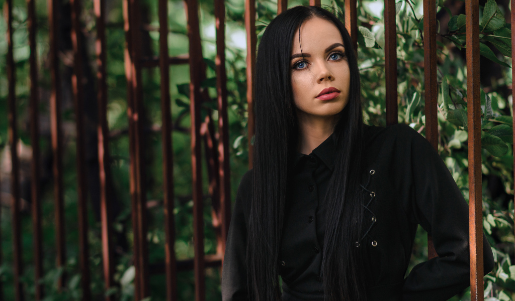 Красивая голубоглазая девушка в черном платье у железного забора