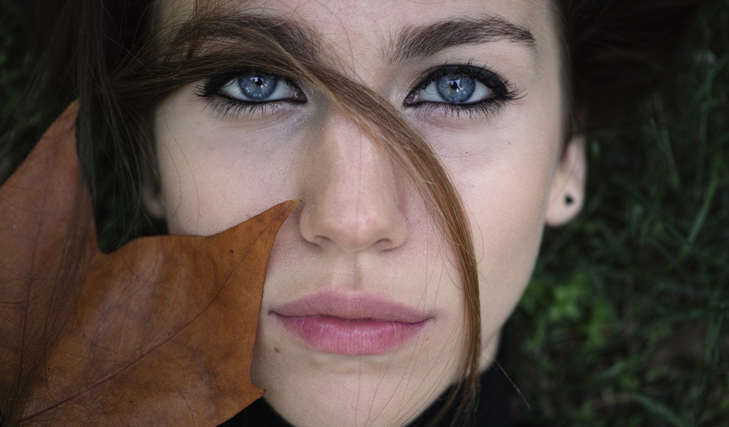 Красивая голубоглазая девушка с желтым листом у лица