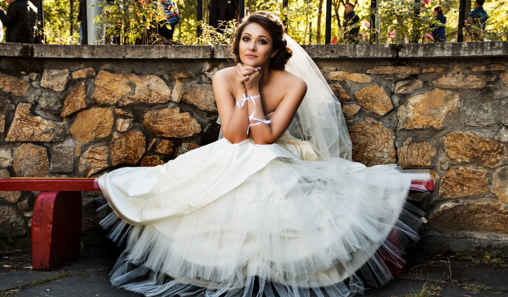 Красивая невеста в белом платье сидит на лавке