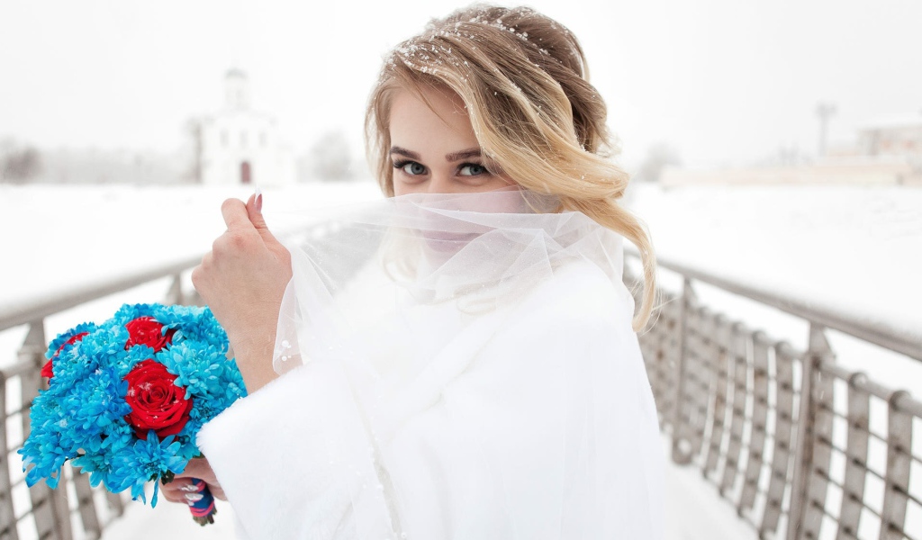 Красивая невеста с букетом в руках закрывает лицо фатой