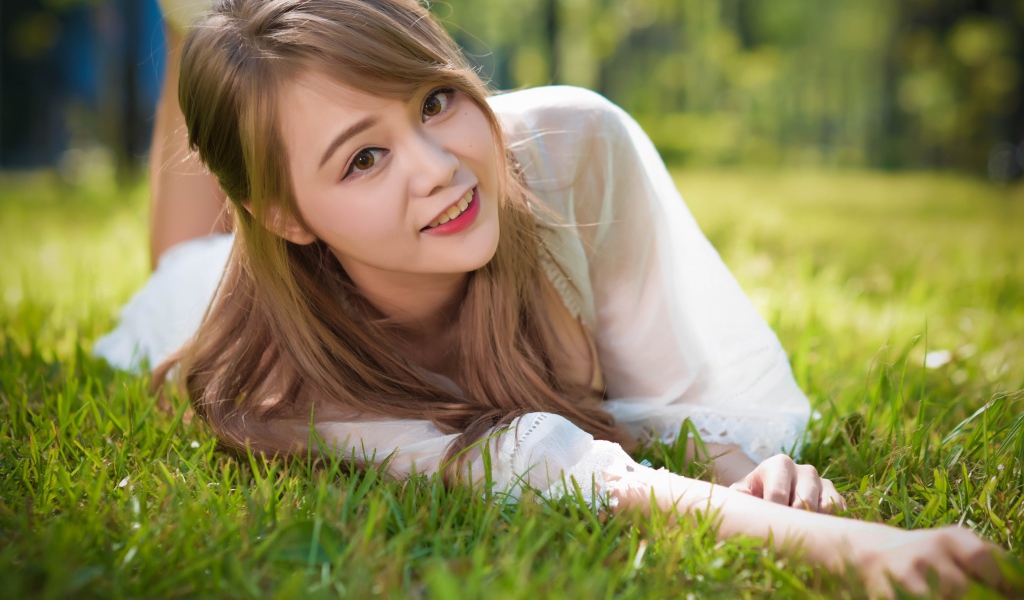 Красивая кареглазая девушка азиатка лежит на зеленой траве