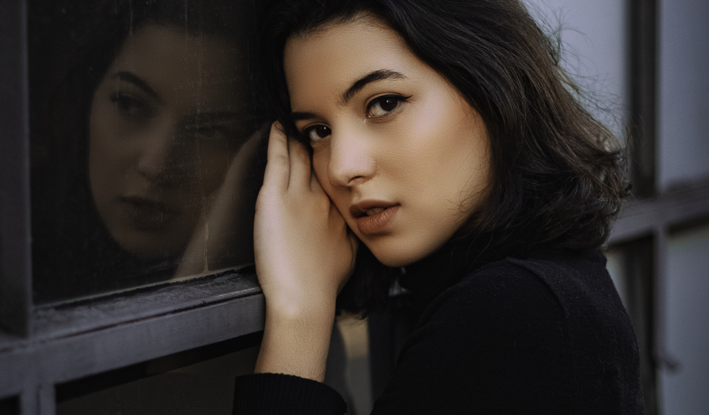 Красивая кареглазая девушка стоит у окна