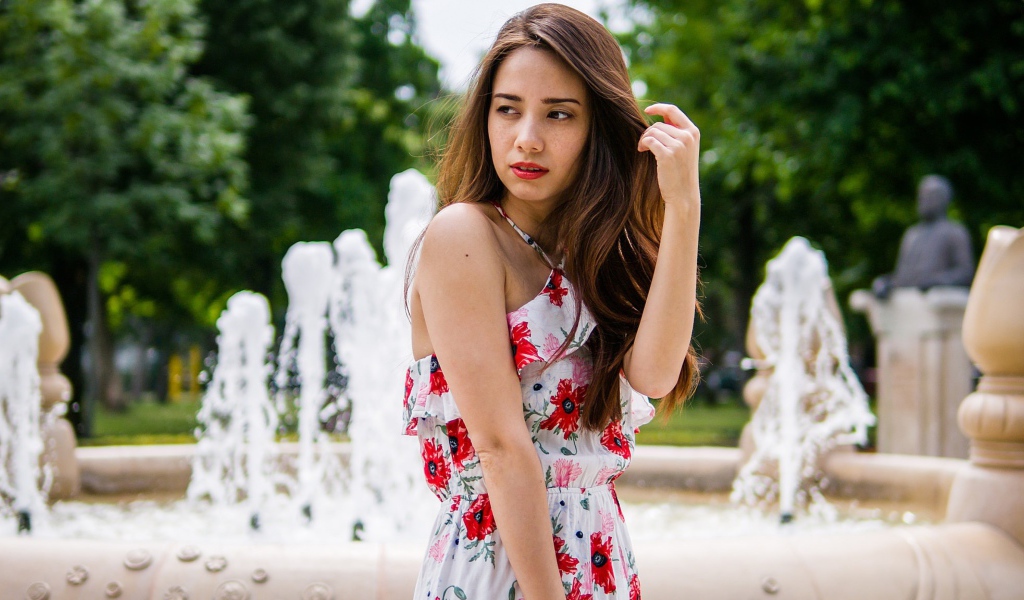 Красивая шатенка в цветастом платье у фонтана летом