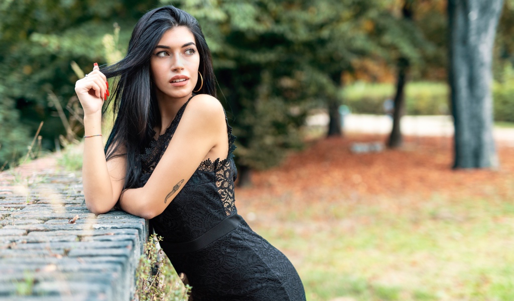 Красивая брюнетка в черном платье в парке