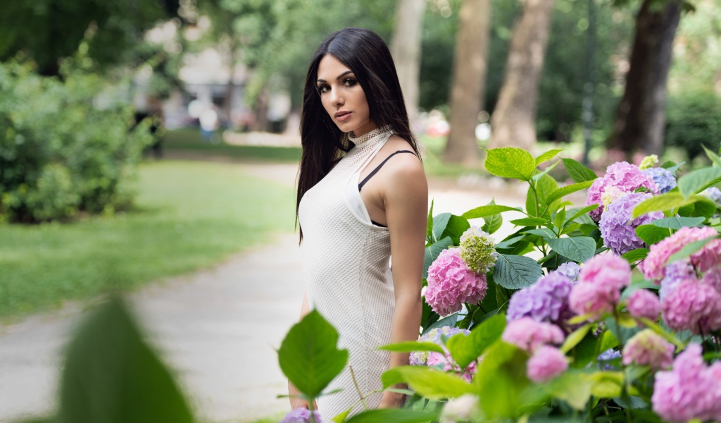 Красивая брюнетка стоит рядом с кустом гортензии