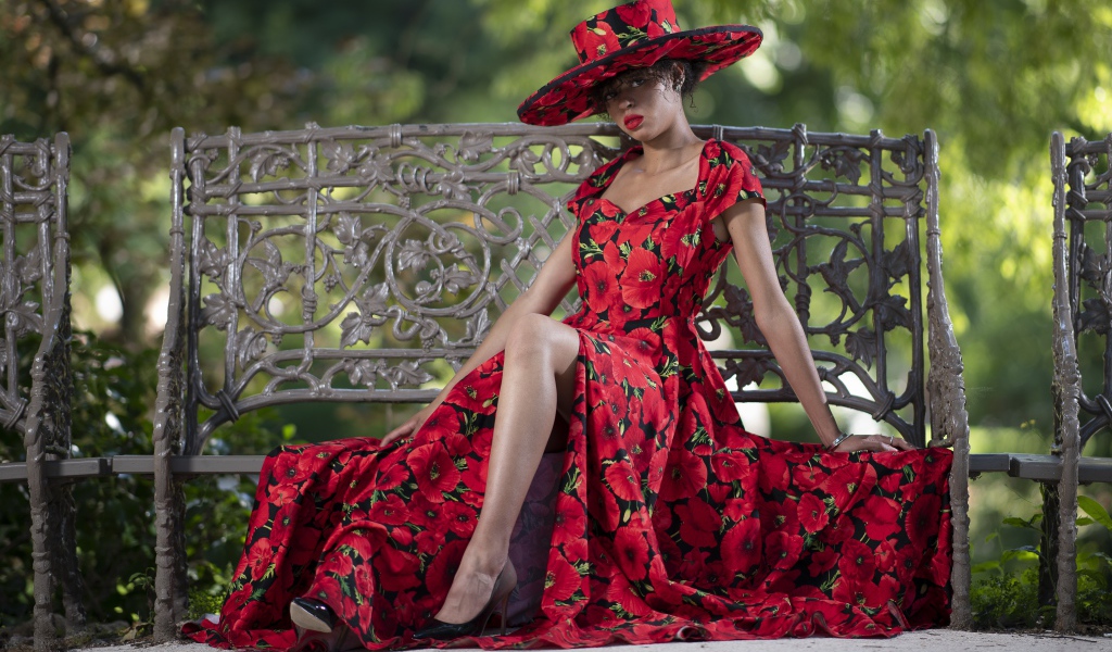 Красивая темнокожая девушка в красном платье сидит на лавке