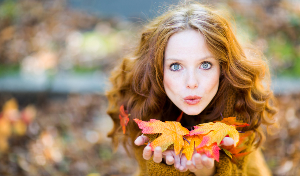 Красивая девушка сдувает листья с ладоней