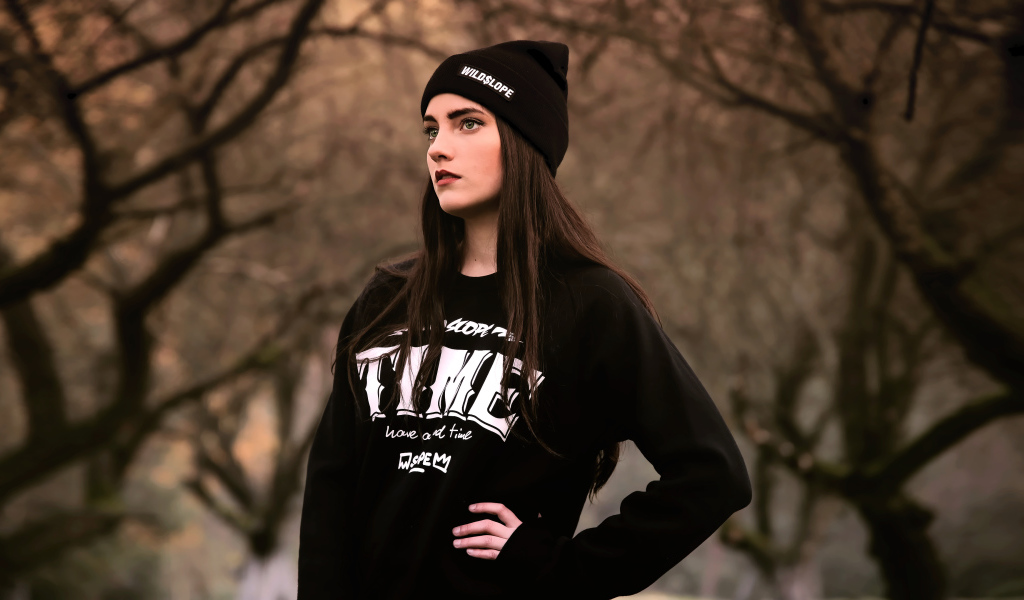 Красивая девушка в черной шапке у деревьев 