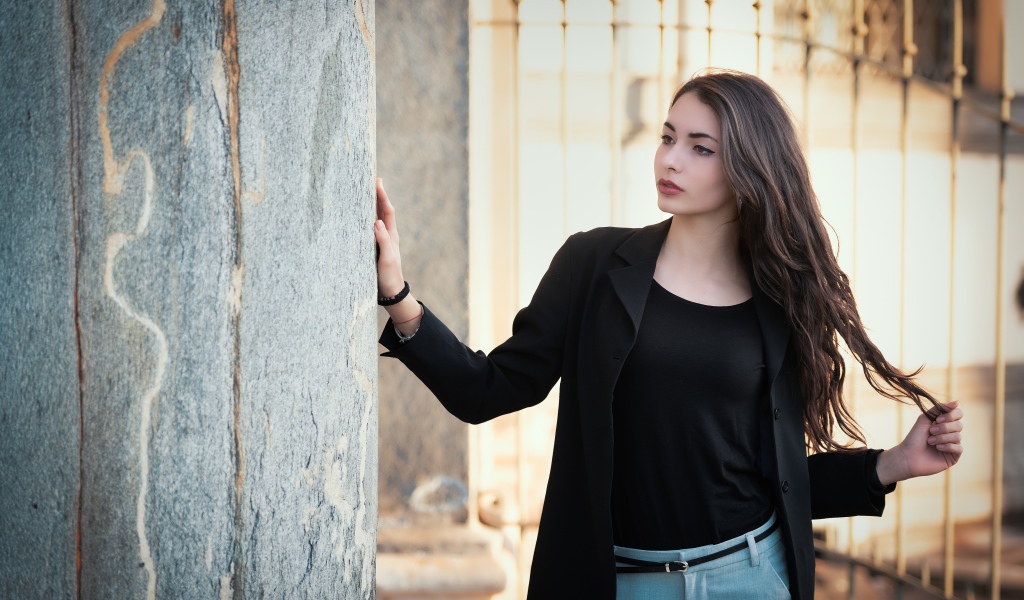 Красивая девушка в черном пиджаке стоит у стены