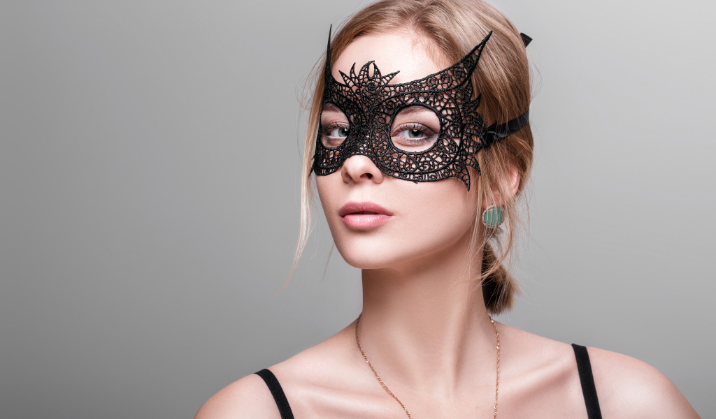 Красивая девушка в черной маске на сером фоне