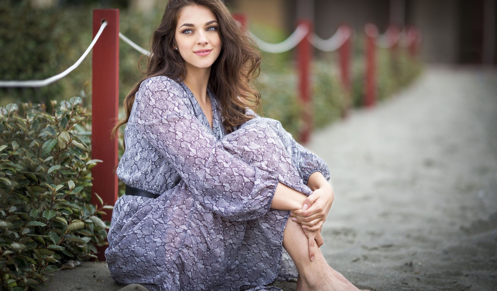 Красивая девушка в платье сидит на песке