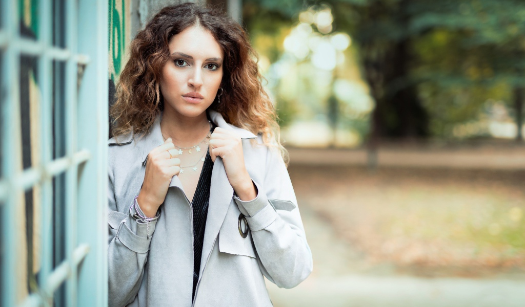 Красивая девушка в сером плаще у стены