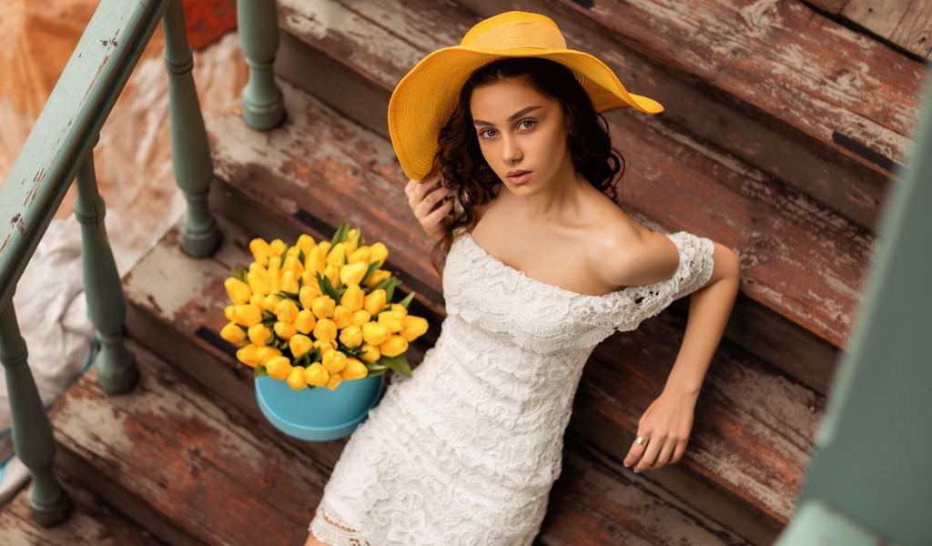 Красивая девушка в белом платье и желтой шляпе на ступеньках с букетом тюльпанов